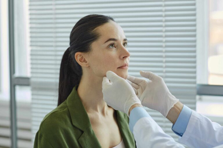 Side view of unrecognizable doctor palpating neck while examining young woman during consultation in clinic or hospital, copy space