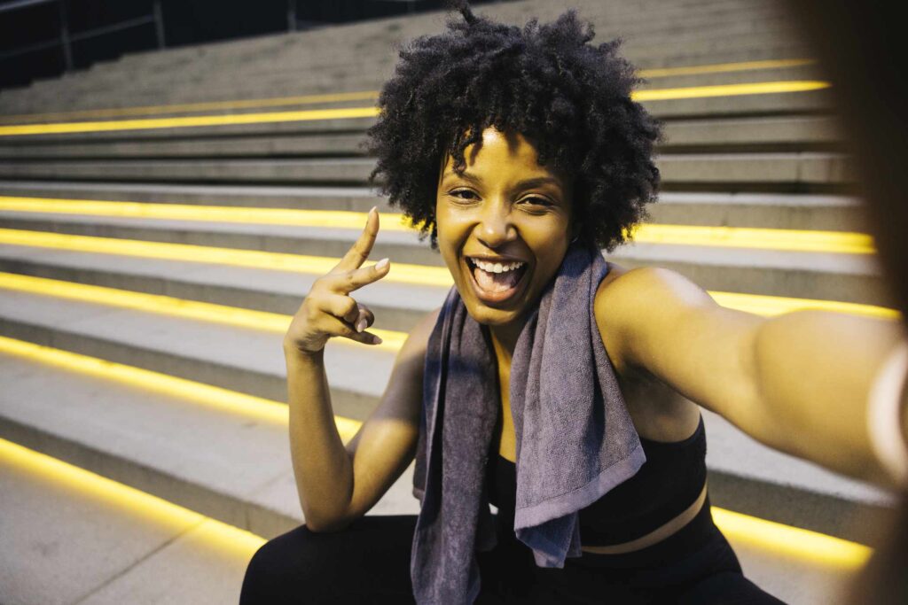 Selfie of a young cheerful woman sitting on illuminated steps, after a workout session in an urban setting.