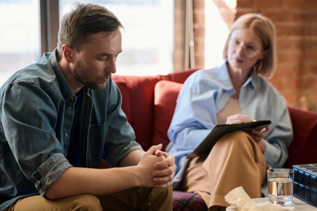 Depressed man having consultation with psychologist, he sitting on sofa and talking about his problems